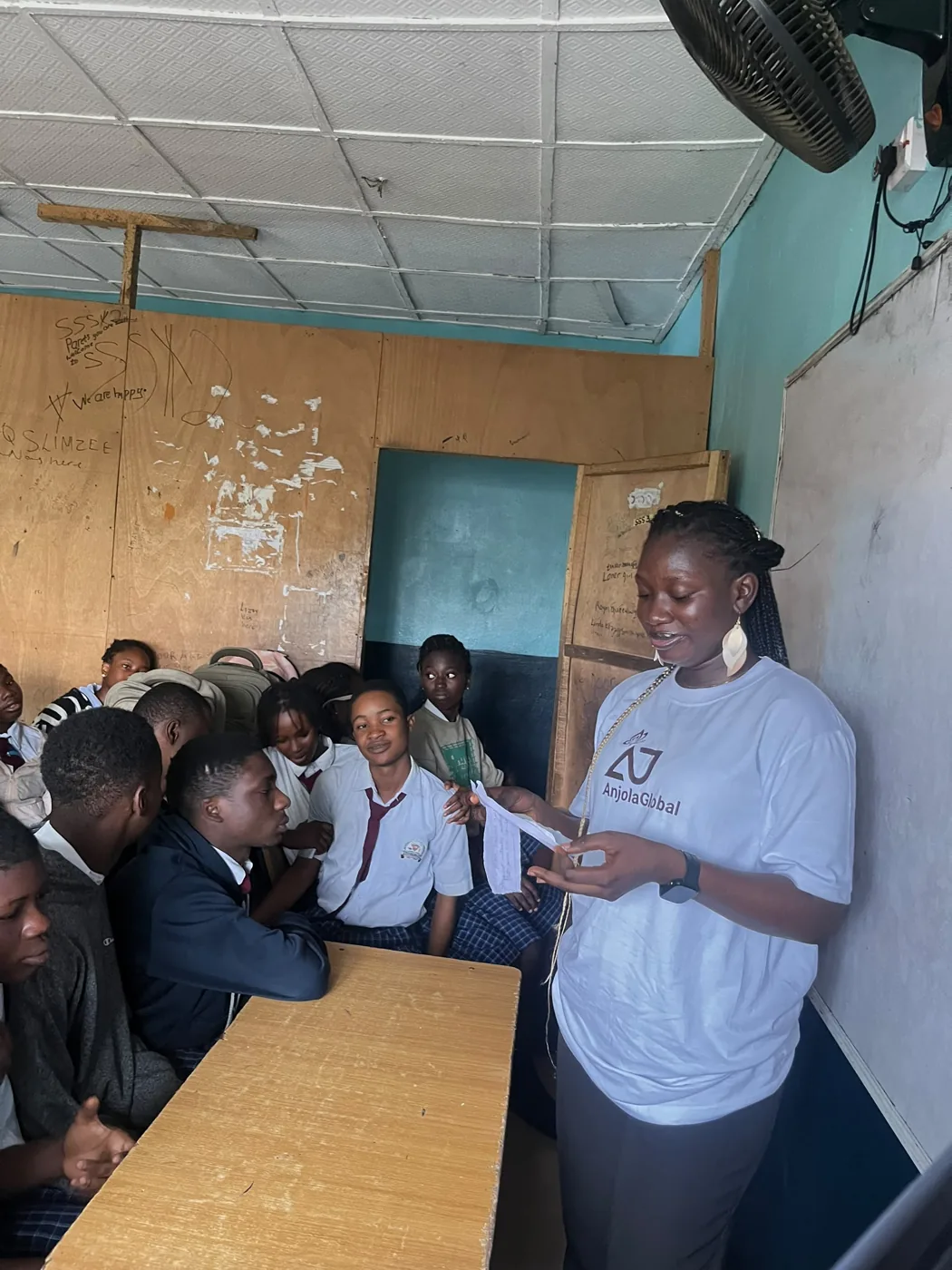Anjola reading a note to a group of students in a classroom